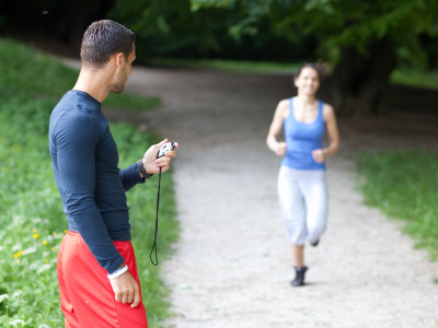 Personal trainer timing a female runner. Selective focus.